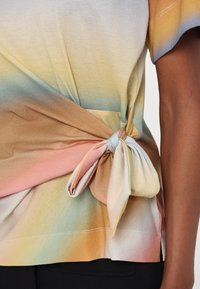 T-shirt multicolore présentant un motif dégradé doux aux teintes de bleu, jaune, pêche et marron, noué à la taille avec un nœud en tissu.