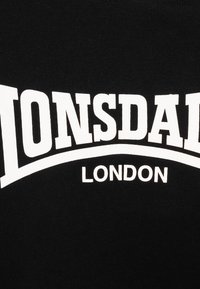 Black cotton t-shirt featuring bold white text "LONSDALE" and "LONDON" in a curved design. Soft texture with standard crew neckline.