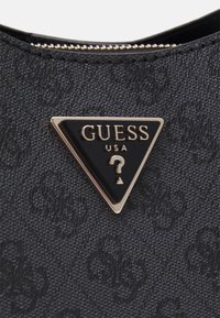 Juodas tekstūruotas audinys su trikampiu Guess logotipu, uždengtu auksine ir juoda spalva, su klaustuku, smulkiai siuvinėtomis detalėmis ir užtrauktuku.
