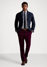 Granatowa marynarka, koszula w kratę, ciemny krawat, bordo spodnie i brązowe buty tworzą formalny strój o zróżnicowanych teksturach i bogatych kolorach.