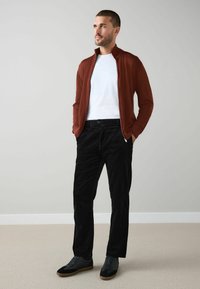 Red zip-up jacket over a white t-shirt, paired with black corduroy pants and black sneakers with gum soles. Plain background.