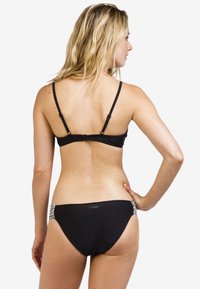 Zwarte bikini met dunne bandjes en een sluiting op de rug, met decoratieve accenten aan de zijkanten. Zachte, gladde textuur.