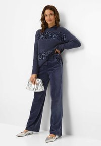 Maglione blu con paillettes, pantaloni di velluto a coste blu larghi, scarpe piatte argento e una borsa a pochette metallica argento. Texture liscia e vestibilità casual.