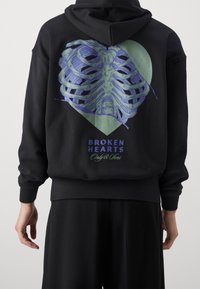Black hooded sweatshirt featuring a ribbed hem and cuffs. The back displays a ribcage graphic in blue and green with "BROKEN HEARTS" text.