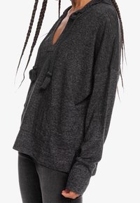 Pullover grigio con cappuccio, scollo a V, tessuto strutturato, fessure laterali e lacci con nappine. Le maniche lunghe arrivano fino ai polsi.