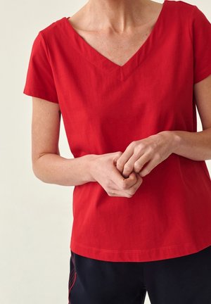 Rød kortærmet top med V-udskæring og glat tekstur. Den har en afslappet pasform og en ren kant, som er parret med sorte bukser.