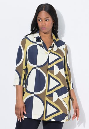 Blouse multicolore avec des motifs géométriques de cercles et de triangles en bleu marine, jaune et marron. Tissu léger avec un col et des manches trois-quarts.