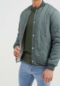 Vadderad, ljusgrön bomberjacka med tryckknappar, ribbade manschetter och en mjuk insida. Kombineras med en mörkgrön T-shirt och jeans.