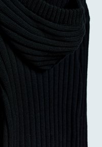 Svart stickad tröja med ribbad textur och cowl-halsringning, som visar ett mjukt och tjockt material med subtila variationer i stygn.