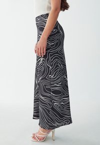Schwarzer Rock mit weißem abstraktem Linienmuster, ausgestattet mit einer taillierten Taille und fließender Silhouette. Kombiniert mit weißen Riemchenheels.