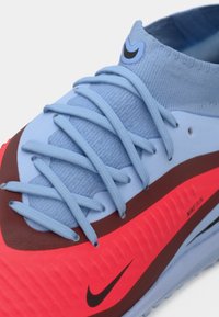 Nike football shoe with light blue upper, red and brown accents, textured finish, flat laces, and a logo on the heel.