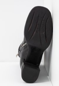 Svart läderstövel med dragkedja liggande på sidan, sula framåt som visar mönster och präglad storlek nummer 42.