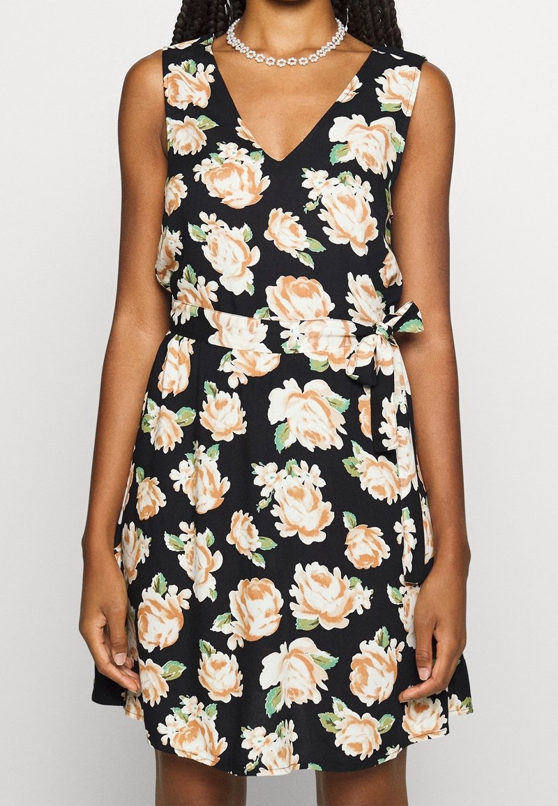 Květinové šaty s černým pozadím, zdobené broskvovými růžemi a zelenými listy. V- výstřih, bez rukávů, s detailem vázání v pase.