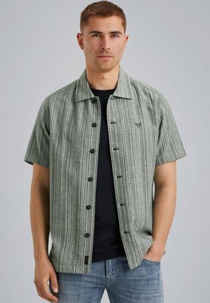 Chemise à manches courtes rayée verte et blanche avec un col boutonné et des boutons noirs, superposée sur un t-shirt noir. Jeans en denim clair présentés.