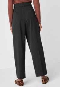 Pantaloni a vita alta e gamba larga in tessuto grigio scuro a righe, caratterizzati da una texture liscia e una vestibilità su misura. Indossati con ballerine con stampa leopardata.