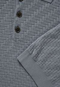 Pull en tricot bleu avec motif en tissage panier texturé, patte de boutonnage avec trois boutons foncés et poignets côtelés aux manches longues.