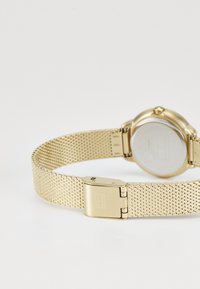 Gold mesh watch with a round case, stainless steel back, and a clasp closure. Smooth texture with an even finish throughout.