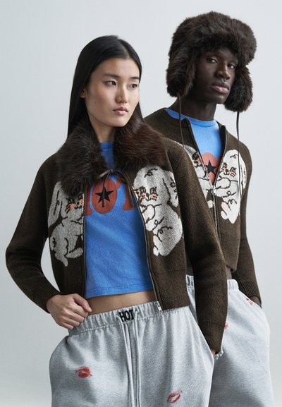 Cardigan marrón de punto con patrón de conejo blanco y cuello de piel; camiseta corta azul con gráfico; pantalones deportivos grises con estampado de labios.