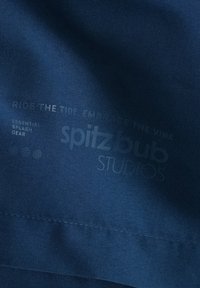 Navyblaues Material mit glatter Textur, bedrucktem weißen Text: "REITE DEN WELLE, UMGAR DIE STIMMUNG" und "spitzbub STUDIOS" mit Icon-Grafiken.