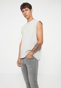 Top senza maniche di un grigio chiaro, realizzato in un tessuto morbido, abbinato a jeans grigi, con una vestibilità slim e dettagli di cucitura discreti.