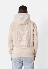 Felpa beige con una grande stampa grafica sul retro, che presenta un sole, serpenti e testo. Realizzata in tessuto morbido con una vestibilità comoda.