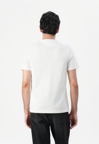 White cotton t-shirt with a crew neckline, short sleeves, and a plain back design paired with black denim jeans, visible pocket stitching.