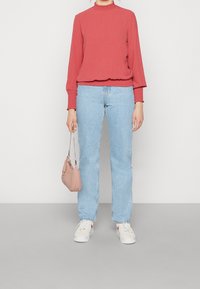 Punainen pitkähihaiset paita, jossa on röyhelökaulus, yhdistettynä vaaleansinisiin suoriin farkkuihin, valkoisiin tennareihin ja pieneen vaaleanpunaiseen laukkua.