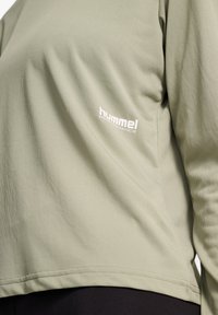 Olivgrünes Langarm-Sportshirt aus strukturiertem Material mit einem weißen "Hummel Performance" Logo auf der linken Seite.