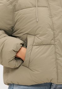 Khačasta puffer jakna s teksturiranim mrežastim uzorkom, s prednjim zatvaračem i velikim bočnim džepovima. Rukavi su preveliki i elastični.