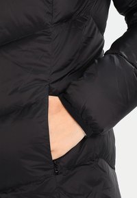 Zwarte gewatteerde jas met een quilted ontwerp, voorzien van een ritszak aan de zijkant, elastische manchetten en een gladde, glanzende stoftextuur.