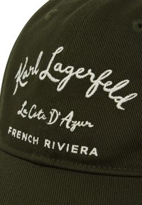 Casquette verte en tissu texturé. Sur le devant, texte brodé en blanc : "Karl Lagerfeld", "La Côte D’Azur" et "French Riviera".