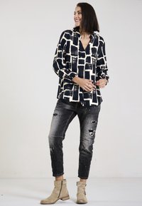 Langärmliges schwarzes Hemd mit einem cremefarbenen Karomuster, kombiniert mit verwaschenen grauen Jeans. Modell trägt beigefarbene Knöchelstiefel.