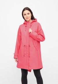 Rosa vattentät regnjacka med huva, dragsko i midjan och två framfickor. Tillverkad av ett slätt, lätt material. Har elastiska ärmslut.