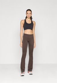 Reggiseno sportivo nero e leggings a campana marroni realizzati in tessuto morbido. L'outfit è completato da scarpe da corsa grigie e rosa con suole nere.