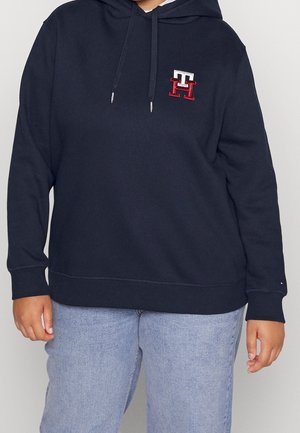 Sudadera con capucha azul marino con detalle de logo en el pecho, hecha de tejido suave, con un corte relajado y bolsillo frontal tipo canguro.