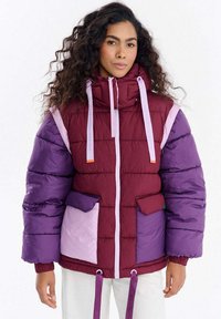 Kurtka pikowana w kolorze bordowym, fioletowym i jasnoróżowym. Posiada wysoki kołnierz, przednie kieszenie oraz ściągacze na sznurki. Tkanina o fakturze z kontrastowymi panelami.