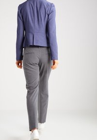 Niebieska, dopasowana marynarka w eleganckim kroju, zestawiona z jasnoszarymi spodniami. Strój uzupełniają białe buty i charakteryzuje się gładką fakturą.