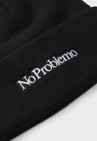 Schwarze Strickmütze mit weicher Textur, die auf der Vorderseite den weißen gestickten Text "No Problemo" zeigt. Einfaches Design ohne zusätzliche Muster.