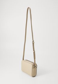 Bežasti pravokutni crossbody torbica s glatkom završnom obradom, podesivim remenom i kontrastnim šavovima. Zatvaranje na zipu na vrhu.