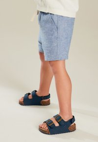 Modre lanene kratke hlače z dvema stranskima žepoma, kombinirane z mornarsko modrimi sandali z dvema zaponkama in podplati s teksturo plute.