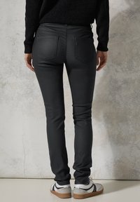 Jeans negros ajustados con una textura suave, dos bolsillos traseros y una cintura alta. Combinados con zapatillas blancas con detalles en negro.