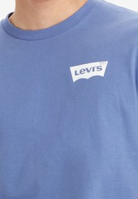 Camiseta de algodón azul con cuello redondo, que presenta un logotipo de Levi's en blanco en el lado izquierdo. Textura suave con un ajuste relajado.