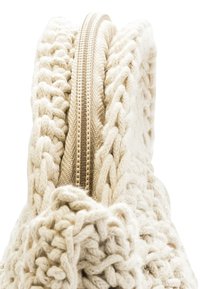 Stickad krämfärgad väska med en texturerad design, utrustad med en guldfärgad dragkedja överst och flätade detaljer längs kanterna.