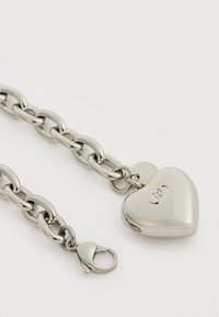 Χοντρό ασημένιο βραχιόλι αλυσίδας με κρεμαστό με σχήμα καρδιάς και κλείσιμο τύπου λαβίδας σε άσπρο φόντο.