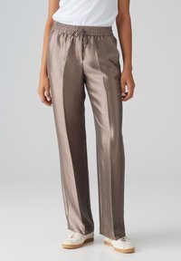 Metallisch bruine wijde broek met een elastische tailleband en trekkoord, met een gladde, glanzende textuur. G gedragen met witte sneakers.