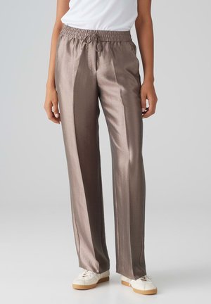 Pantalons amples métalliques marron avec une taille élastique et un cordon de serrage, affichant une texture lisse et brillante. Portés avec des baskets blanches.