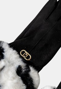 Guanti neri in tessuto morbido, con un polsino in pelliccia sintetica bianca con un motivo nero e un dettaglio in hardware dorato al polso.