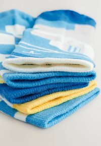Hög med strumpor i olika nyanser av blått, vitt och gult. Tillverkade av mjukt, texturerat material med grafiska mönster.