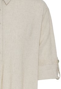 Smėlinės spalvos lininė palaidinė su sagų užsegimu, apykakle ir rankovėmis, sukeltomis ir prilaikomomis sagomis prie blakstienų.