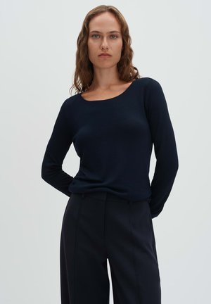 Navy long-sleeve top with a scoop neckline, made from a smooth material. Paired with tailored black trousers, emphasizing a sleek silhouette.